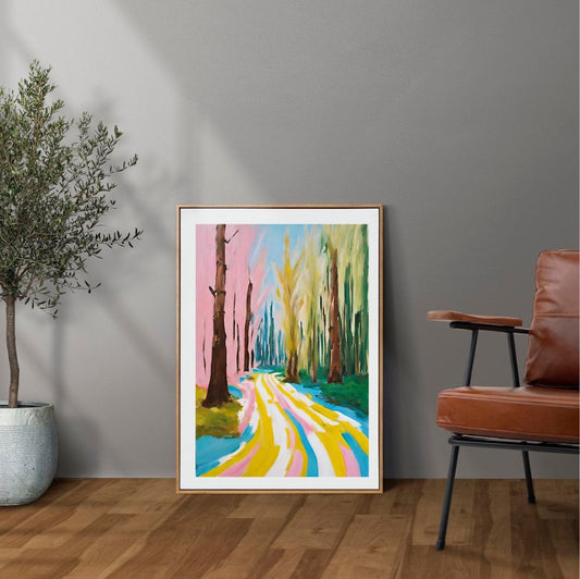 Framed abstract artwork of a colorful forest path on a gray wall with a plant and chair in the foreground.