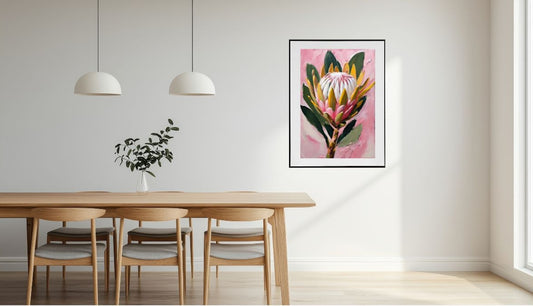 Framed floral Pink Protea flower artwork on a wall above a dining table with chairs.