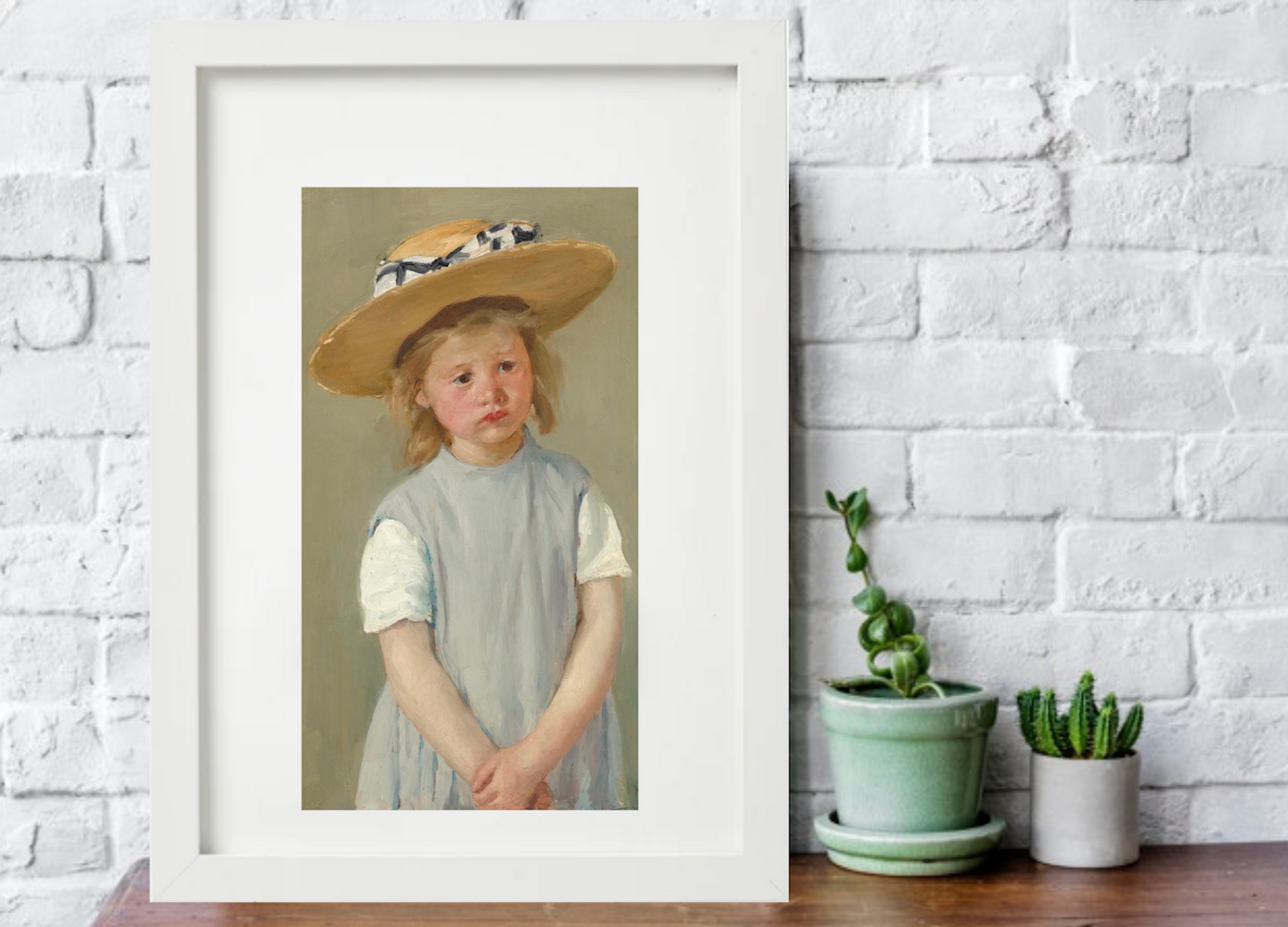 little girl in straw hat and grey dress vintage art print framed in white on table