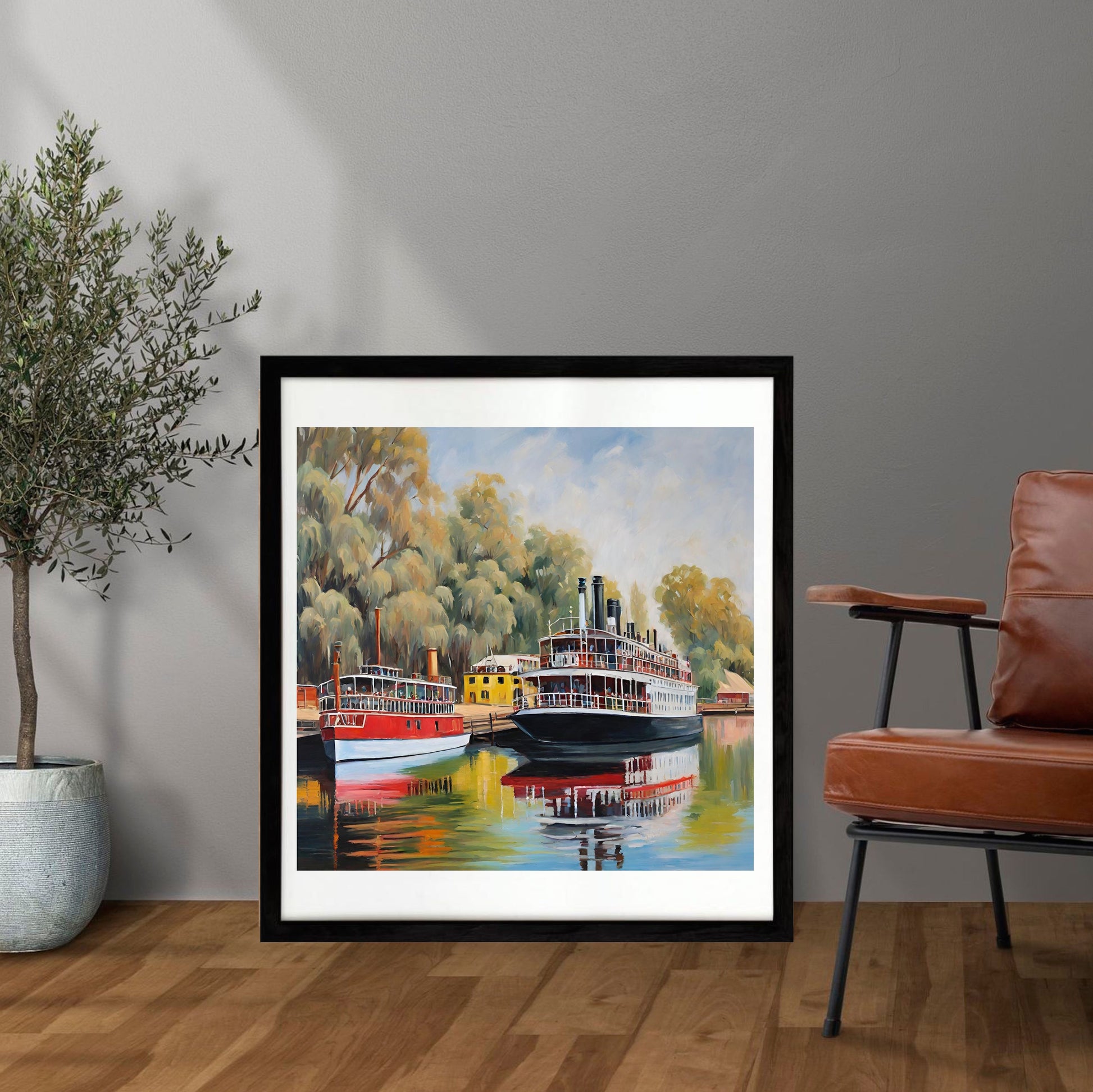 Framed painting of a river scene with paddle steamers in a room with a plant and chair.