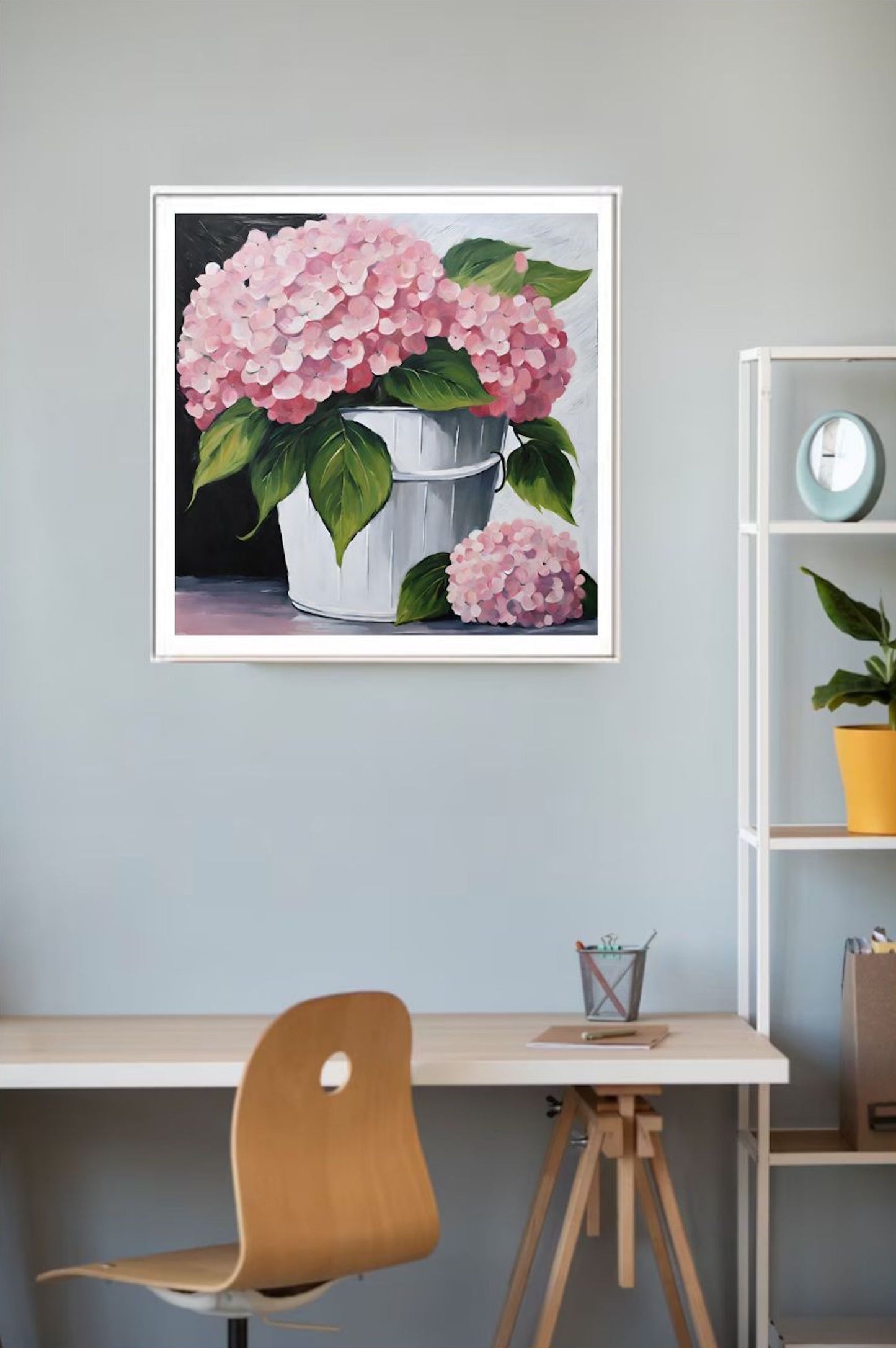 Framed artwork of pink Hydrangea flowers in a white  bucket on a wall above a desk.