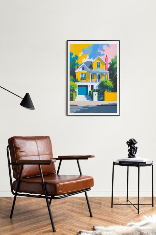 Living room with a brown leather chair, side table, and colorful yellow house painting framed and hung on wall on the wall.