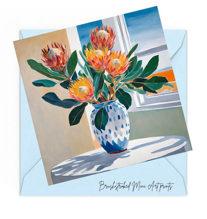 pink and orange proteas flowers in blue and white ceramic vase on white table near window mini art print.