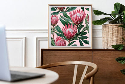 Pink proteas and green leaves framed art print with pink background framed and sitting on table